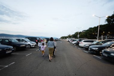 Anne ve çocuklar alacakaranlıkta şehrin otoparkında yürüyorlar..