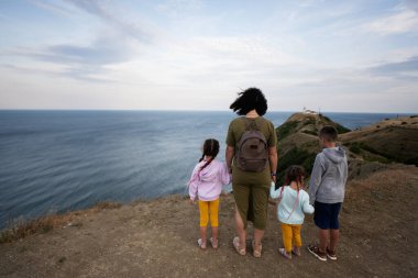 Anne ve üç çocuk bir dağın tepesinde durup denize bakıyorlar. Cape Emine, Karadeniz kıyısı, Bulgaristan.