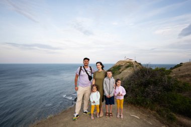 Arka planda deniz feneri olan mutlu bir aile dağın tepesinde. Cape Emine, Karadeniz kıyısı, Bulgaristan.