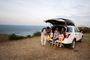 Mutlu bir aile sahildeki bir karavan cipinin bagajında oturuyor. Cape Emine, Karadeniz kıyısı, Bulgaristan.