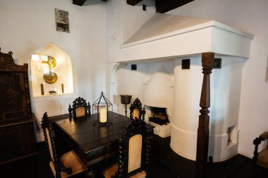 Bran, Brasov, Romanya- Haziran 2023: Köhne ahşap masa, antika sandalyeler ve şömineli geleneksel ortaçağ şatosu yemek odası. Özgün tarihi iç dekorasyon.