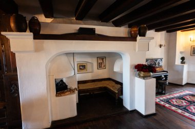 Bran, Brasov, Romanya- Haziran 2023: Beyaz şöminesi, klasik piyanosu ve tavanında ahşap kirişleri olan geleneksel bir şato. Dekoratif elementlerle sıcak ve davetkar atmosfer.