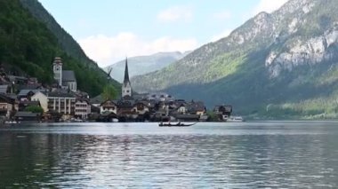 Avusturya Alpleri 'ndeki resim gibi bir göl köyü. İnsanlar güneşli bir günde güzel dağ manzaralı bir tekne gezisinden hoşlanırlar..