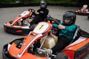 Miğferli iki çocuk açık havada go-kart yarışıyor, eğlence ve heyecan yaşıyorlar..