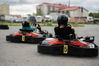 Miğferli iki çocuk açık havada go-kart yarışıyor, eğlence ve heyecan yaşıyorlar..