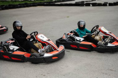 Miğferli iki çocuk açık havada go-kart yarışıyor, eğlence ve heyecan yaşıyorlar..