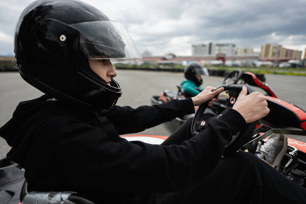 Close-up of a focused person in a black helmet driving a go-kart during an intense race. Experience the thrill and excitement of go-kart racing.