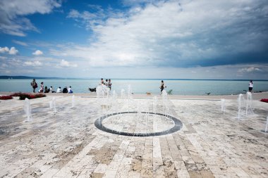 Halka açık bir su çeşmesi olan güzel bir sahil gezisi. İnsanlar deniz kenarında güneşli bir günün tadını çıkarıyorlar..
