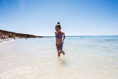 Güneşli bir günde sahilde oynayan genç bir kız. Hırvatistan 'ın Zaton kentinde berrak suyun ve açık mavi gökyüzünün tadını çıkarıyor..