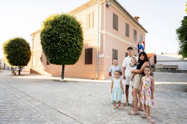 Hırvatistan 'ın Nin kentinde ağaçlı ve bayraklı şeftali renkli bir binanın önünde bir araya gelip gülümseyen neşeli bir aile..
