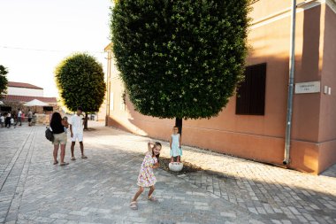 Hırvatistan 'ın Nin kentinde güneşli bir günde güzel şekilli bir ağacın altında oynayan neşeli çocuklar..