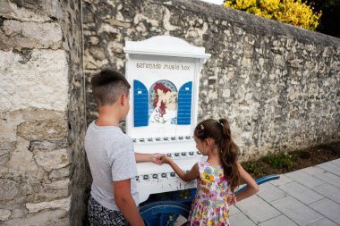 İki çocuk serenat yapan bir müzik kutusuyla, güneşli bir günde kırsal bir duvarın yanında melodik bir anın tadını çıkarıyorlar..