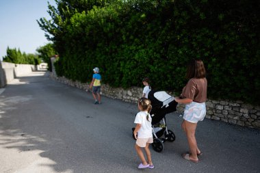 Güneşli bir günde çocuklar ve bebek arabasıyla dışarıda yürüyüş yapan bir aile. Hırvatistan 'ın Nin kentinde yeşil alanla çevrili manzara yolu.