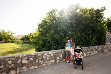 Sevgi dolu bir anne ve üç çocuğu güneşli bir günü Hırvatistan 'ın Nin kentindeki yemyeşil arka planda taştan bir duvarın yanında geçirdiler..