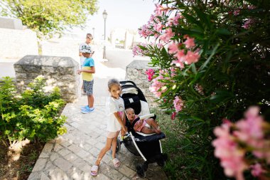 Çocuklar güneşli bir günde bebek arabasında, Hırvatistan 'ın Nin kentinde çiçek açan çiçeklerle çevrili canlı bir bahçeyle dışarıda eğleniyorlar..