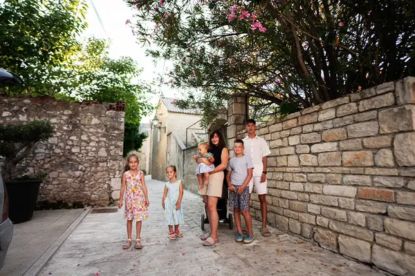 Birkaç çocuklu mutlu bir aile dışarıda güneşli bir günün tadını çıkarıyor. Büyüleyici bir taş duvarın yanında. Gülen yüzler, günlük kıyafetler ve sıcak ışıklandırma Hırvatistan 'ın Nin kentinde neşeli bir atmosfer yarattı.