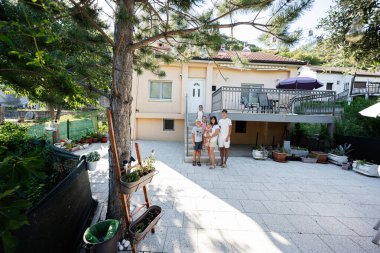 Aile bahçelerinde mutlu bir şekilde poz veriyor. Parlak güneşli bir gün, yeşillik ve saksı bitkileriyle, açık havada bir yaşam alanı sergiliyor..