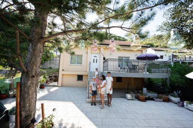 Neşeli aile arka bahçelerinde toplanır, dekoratif ışıkları sarkan ve rahat evlerini çevreleyen yemyeşil bir yaz gününün tadını çıkarırlar..
