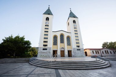 Seçkin ikiz kuleleri ve saat yüzleri olan zarif Aziz James kilisesi cephesi. Medjugorje 'de berrak mavi bir gökyüzü altında sakin bir ortamda klasik mimarinin güzelliğini yakalar..