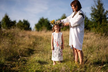 Bir kadın sevgiyle genç kızlarına taç takıyor. Güneşli bir çayıra. Doğanın temalarını çağrıştırıyor.