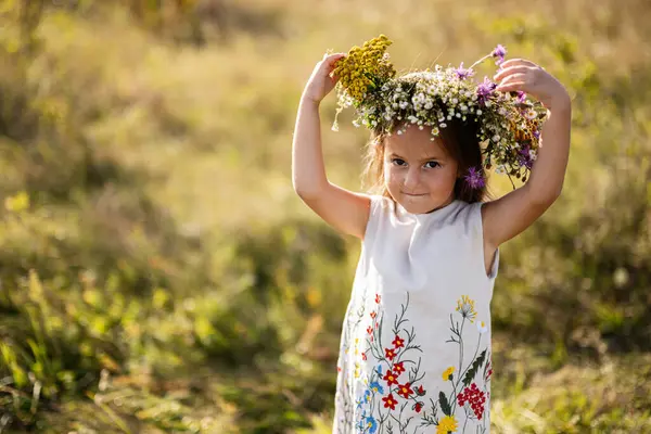 Genç bir kız güneşli bir çayırda renkli bir çiçek tacı giyerek doğanın tadını çıkarıyor. Doğal bir ortamda masumiyet ve neşeyi somutlaştırıyor..
