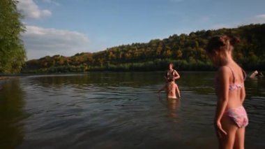 Bir aile güneşli bir günün tadını çıkarır, yüzmek ve nehirde oynamak. Çocuklar anneleriyle suda yürüyorlar, bir çocuk da kameraya bakıyor.. 