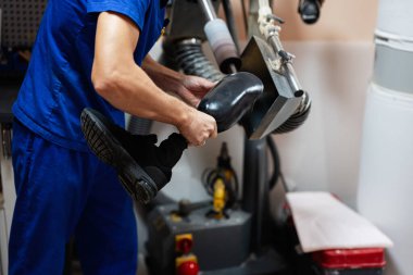 Mavi tulum giyen yetenekli bir teknisyen atölye ortamında özel ekipman kullanarak protez bacağını dikkatlice parlatıyor..