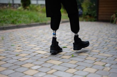 Protez bacaklar kullanan bir insan kaldırım taşı yolunda ileri doğru adım atar. Açık havada güç, hareketlilik ve esnekliği simgeler..