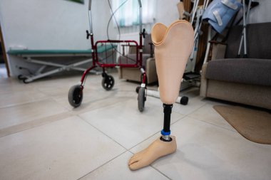 Bir rehabilitasyon merkezinde yürüyen bir adamın yanındaki fayanslı zemine yerleştirilmiş protez bacak, fiziksel zorlukların üstesinden gelen bireylerin gücünü ve hareketliliğini simgeliyor..