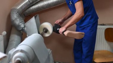 Mavi üniformalı yetenekli bir teknisyen, bir atölye ortamında ustalık ve ustalığı vurgulayan özel makineler kullanarak protez bacağını dikkatlice parlatıyor..