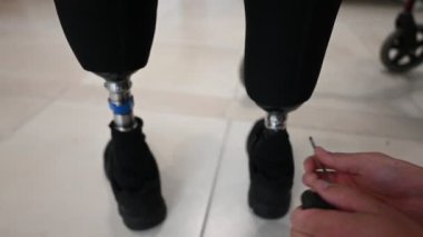 Bir teknisyenin protez bacaklara ayarlamalar yapması, rehabilitasyon ortamında hassasiyet ve özen göstermesi. Görüntü yenilikleri ve kişisel tıbbi desteğin önemini aktarır.