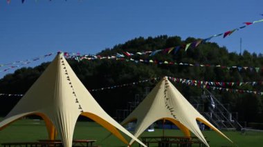Güneşli, mavi bir yaz gününde renkli bayraklı iki boş çadır. Festivalin başlamasını bekliyorum..