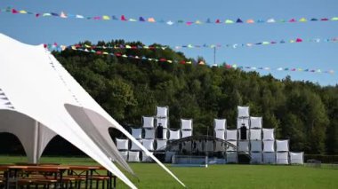 Büyük bir açık hava sahnesi ve festivalde beyaz bir çadır. Sahnenin arkasında büyük bir orman alanı var..
