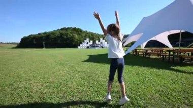 Mutlu küçük bir kız güneşli bir yaz gününde bir parkta neşeyle zıplıyor. Heyecanlı ve eğleniyor..