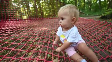 Sarışın ve beyaz tişörtlü tatlı bir kız bebek ormanda kırmızı bir ağda oturmuş, merakla ve merakla etrafına bakıyor. Ebeveynlik, çocukluk ya da açık hava eğlencesi için mükemmel.