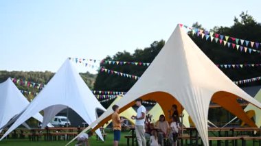 Aileler ve arkadaşlar bir açık hava festivalinde toplanıp sosyalleşiyorlar. Aralarına renkli bayraklar asılmış beyaz ve yanık tenli çadırlar kurulmuştur. Piknik masaları çadırların etrafındaki çimlerin üzerinde..
