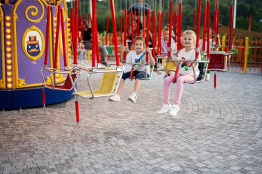 Bir grup mutlu çocuk lunaparkta atlıkarınca salıncağında eğleniyor. Gülümseyen çocuklar aydınlık bir günde dışarıda eğleniyorlar..