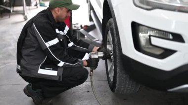 Üniformalı bir tamirci araba lastiğindeki fındıkları sökmek için İngiliz anahtarı kullanıyor. Sonra lastiği çıkarır ve yenisini takmaya hazırlanır.. 