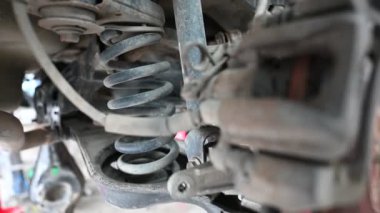 Otomotiv garajında tamir edilen bir arabanın süspansiyon sisteminin yakın çekim görüntüsü. Tamirciler, aracın güvenli ve pürüzsüz bir şekilde kullanılması için yıpranmış parçaları değiştirmeye çalışıyorlar..
