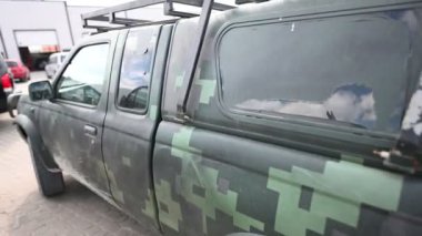 Çatı rafı olan dayanıklı, pikselli bir kamuflaj kamyonu güneşli, parçalı bulutlu bir günde asfalt bir otoparkta park halindedir..