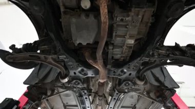 Araba tamirhanesinde hidrolik asansörle kaldırılan bir arabanın altında. Otomotiv, araba tamiri ve bakımla ilgili içerik için mükemmel.