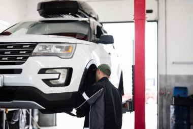 Bir tamirci son model bir garajda bulunan beyaz bir Amerikan cipini inceliyor. Konferansta otomotiv bakımı, onarım uzmanlığı ve temiz, parlak bir atölyede profesyonel hizmet üzerinde duruluyor..