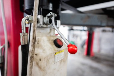 Detailed view of a red-handled lever and hydraulic equipment in an industrial workshop, highlighting machinery mechanics and engineering tools. clipart