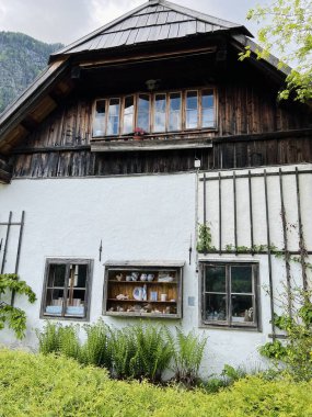 Koyu ahşap aksanlı, yeşil yapraklarla çevrili ve Avusturya 'nın Hallstatt şehrinde sergilenen çömlek sergilenen antika pencereli güzel bir kır evi. Sahne bir sükunet ve tarih hissi uyandırıyor..