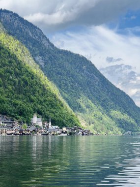 Avusturya 'nın Hallstatt şehrinde huzurlu ve resimsel bir manzara yaratan, yemyeşil dağlarla çevrili, sakin bir göl ve bulutlu bir gökyüzü, güzel bir köy..