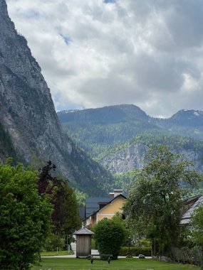 Bu sakin görüntü, Avusturya 'nın Hallstatt şehrinde güzel bir dağlık alana kurulmuş, bulutlu bir gökyüzünün altında dramatik dağlar tarafından çerçevelenmiş, büyüleyici evleri çevreleyen, huzurlu ve huzurlu bir atmosfer sunan tuhaf bir köyü yakalıyor..