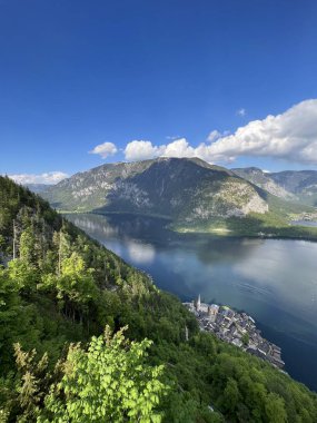 Avusturya 'nın Hallstatt kentindeki berrak mavi gökyüzünün altında yemyeşil tepeler ve görkemli dağlarla çevrili el değmemiş masmavi bir göl ile çevrili çarpıcı bir dağ manzarası..