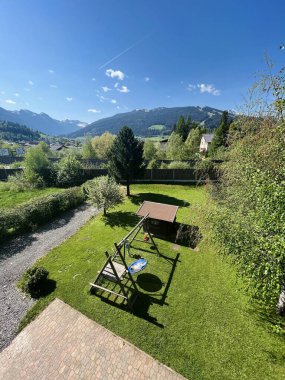 Salıncak, yemyeşil yemyeşil ve açık mavi gökyüzünün altındaki dağların yer aldığı Idyllic arka bahçe sahnesi. Huzur, aile eğlencesi ve doğal güzellik kavramları için mükemmel..