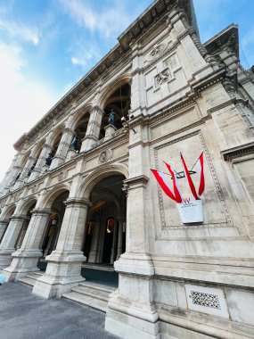 Bu resim, Avusturya 'nın Schonbrunn Sarayı' ndaki açık mavi gökyüzünün altında canlı yeşil yeşilliklerle çerçevelenmiş büyük tarihi bir binanın resimli bir görüntüsünü yakalar. Sahne sükunet ve mimari zarafet yayar..