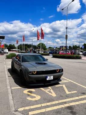 Brno, Çek Cumhuriyeti - 22 Mayıs 2022: Gri renkli, kaslı Dodge Challenger R / T 5.7, güneşli bir alışveriş merkezine park edilmiştir. Parlak bayraklar ve mavi bir gökyüzü canlı atmosferi güçlendirir..